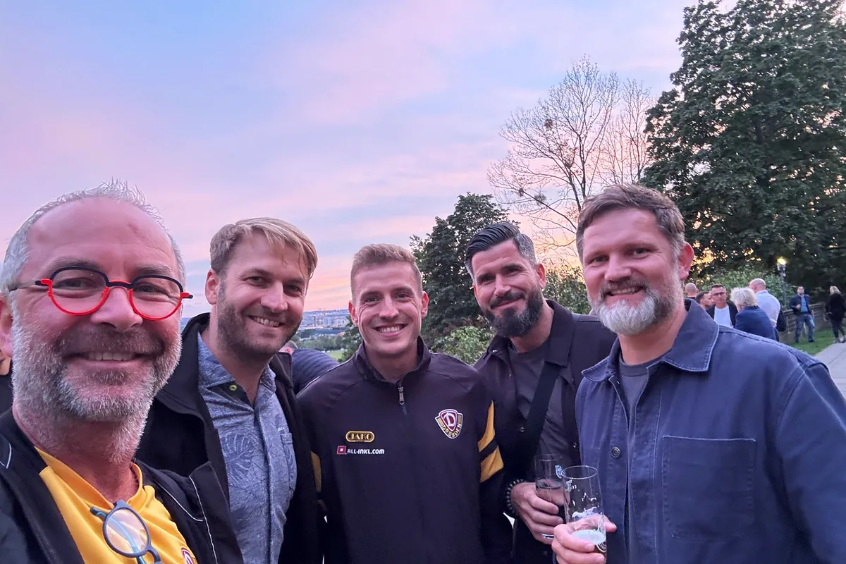 Fünf lächelnde Gäste des Sponsorenabends der SG Dynamo Dresden, eine Person in Dynamo-Trainingsjacke, vor rosa Abendhimmel über Dresden